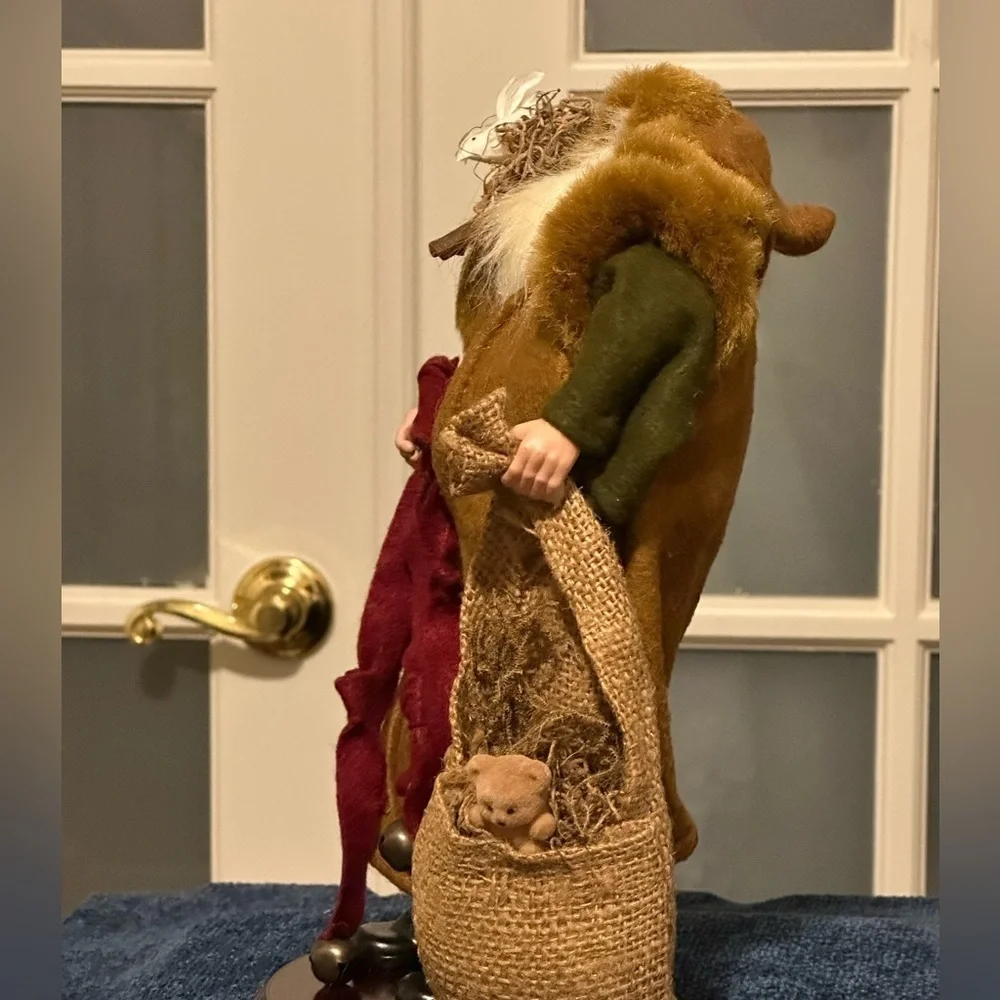 Shaggy haired and bearded Santa wears a brown cape and carries a burlap sack.